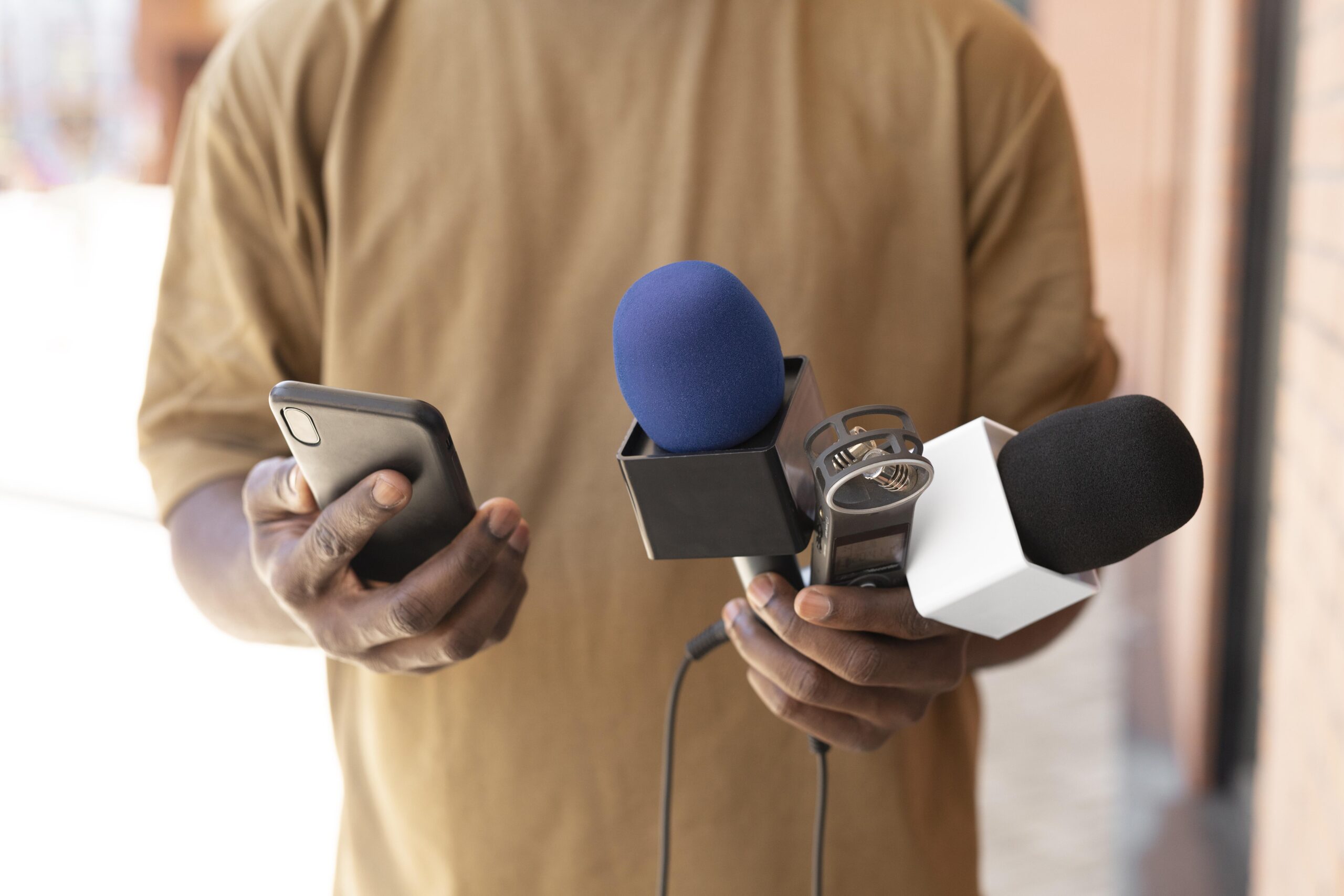 Manos que sostienen un teléfono móvil a la izquierda y dos micrófonos a la derecha, alineando el discurso de la empresa sobre la gestión de crisis.